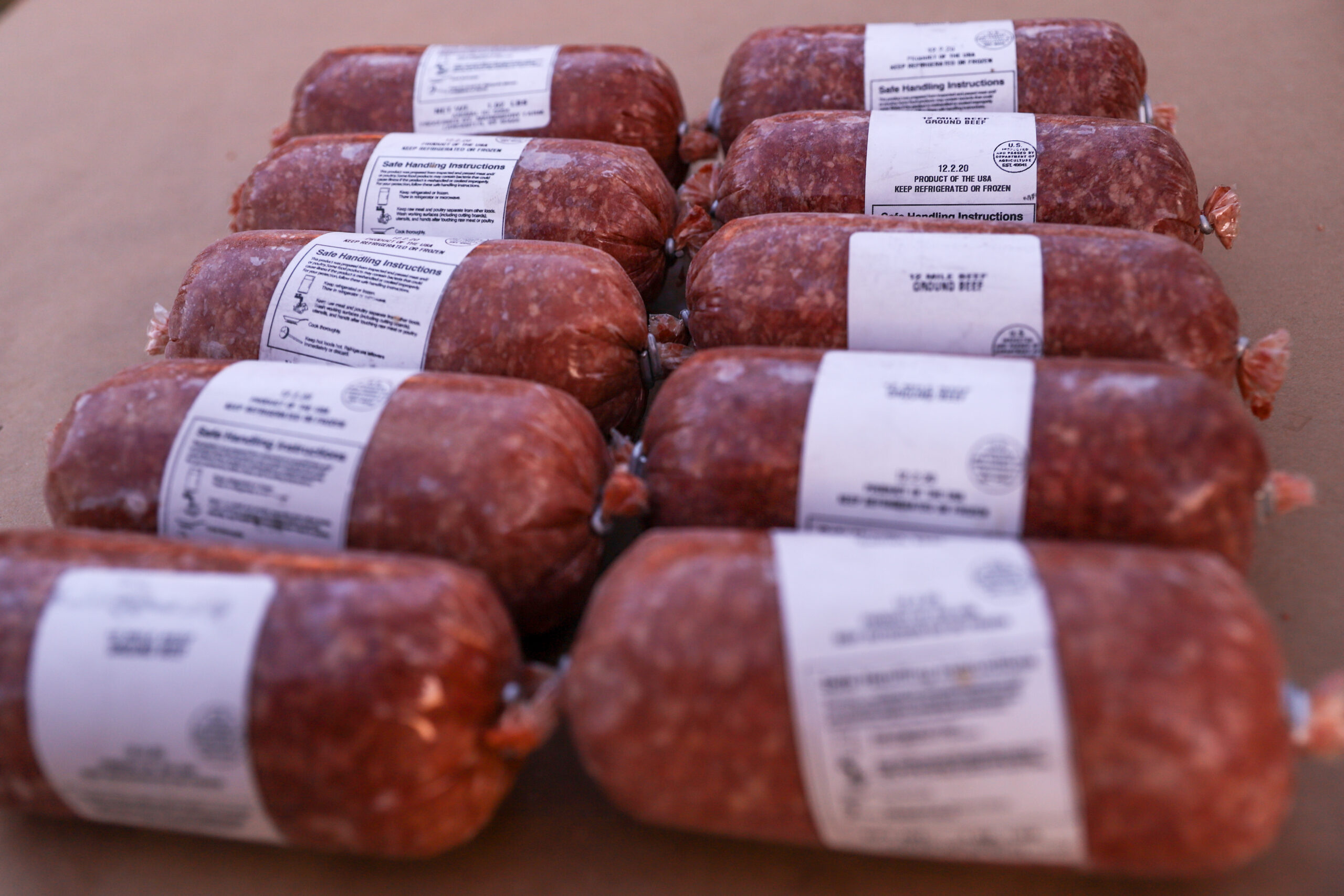 Packages of ground beef with labels displaying safe handling instructions, arranged neatly on a brown surface.
