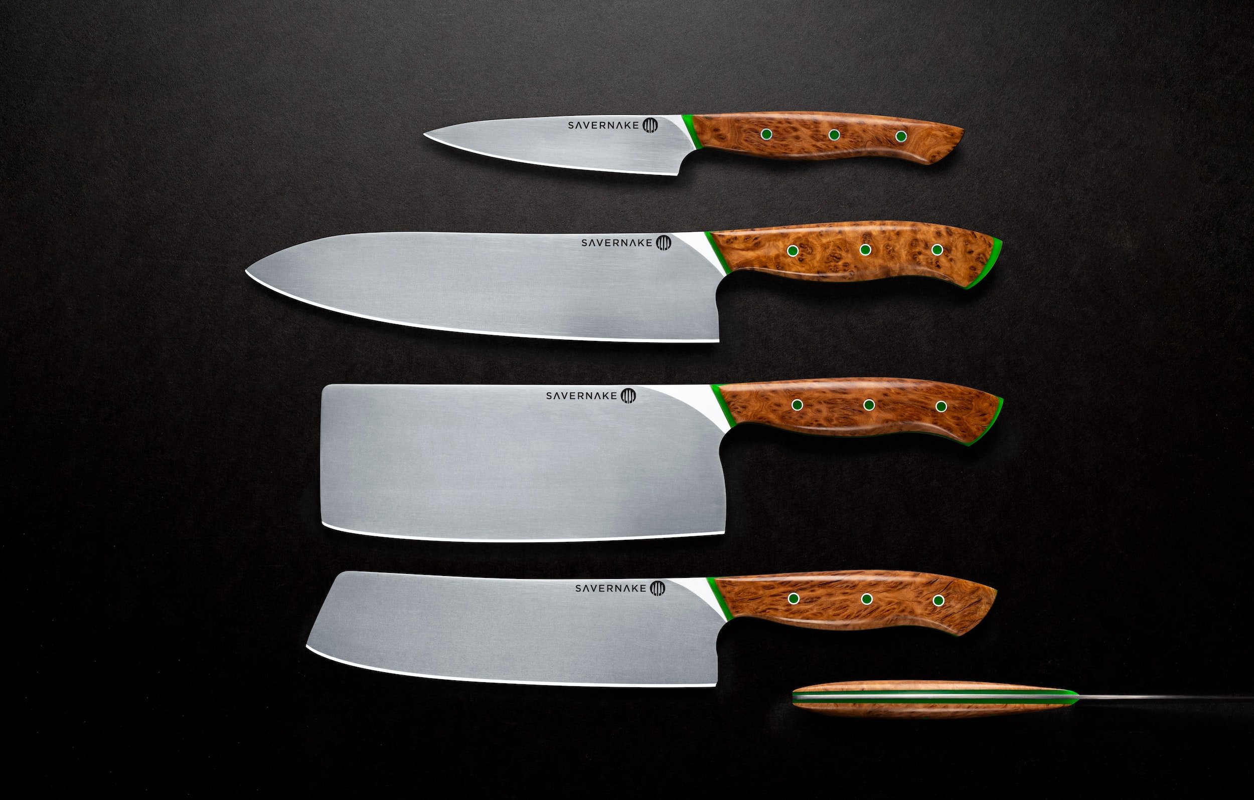 unsplash-image-tyDgjiJbz54 A set of four high-quality kitchen knives arranged on a dark surface, featuring stainless steel blades and elegant wooden handles with green accents. The knives include a chef's knife, a paring knife, and two cleavers, showcasing craftsmanship and design by Savernake.